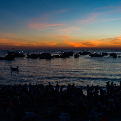 Hình ảnh chợ cá Tam Tiến ở Quảng Nam vào lúc bình minh với nhiều tàu thuyền trên biển và đông người mua bán trên bờ. Khung cảnh tạo cảm giác yên bình và sống động của một phiên chợ cá truyền thống miền Trung.