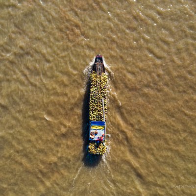 Ảnh chụp trên cao một chiếc thuyền chở đầy trái cây đang di chuyển trên sông Tiền Giang. Cảnh vật tạo cảm giác yên bình và tĩnh lặng giữa dòng sông rộng lớn.