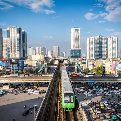 Hình ảnh chụp một nút giao thông đô thị đông đúc với tàu điện trên cao và nhiều phương tiện giao thông dưới đường. Cảnh quan thể hiện sự nhộn nhịp và hiện đại của thành phố vào buổi chiều.