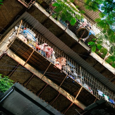 Bức ảnh chụp một toà nhà tập thể cũ với các ban công có hàng rào kim loại và cây xanh xung quanh. Không gian mang lại cảm giác yên bình và gần gũi với cuộc sống đô thị hàng ngày.