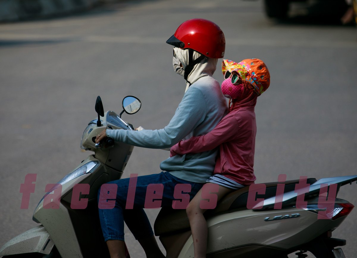 Bức ảnh chụp hai người trên xe máy, đều mặc đồ bảo vệ và đeo khẩu trang, mũ bảo hiểm để tránh ô nhiễm và bụi bẩn. Cảnh tượng tạo cảm giác bình yên nhưng cũng gợi lên sự cần thiết của việc bảo vệ sức khoẻ trong môi trường đô thị.