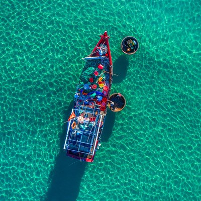 Bức ảnh chụp toàn cảnh trên không một chiếc thuyền đánh cá truyền thống trên vùng biển trong xanh. Khung cảnh tạo cảm giác bình yên và tĩnh lặng với ánh sáng tự nhiên dịu nhẹ chiếu xuống mặt nước.