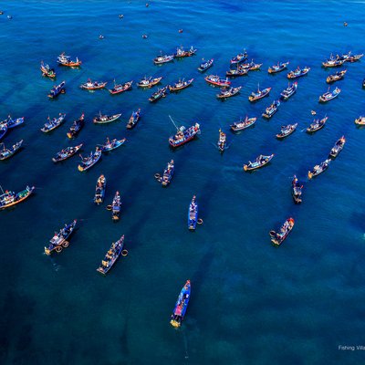Hình ảnh toàn cảnh trên không của một làng chài với nhiều thuyền đánh cá trên biển xanh. Cảnh biển rộng lớn và yên bình tạo cảm giác thư thái và tĩnh lặng.