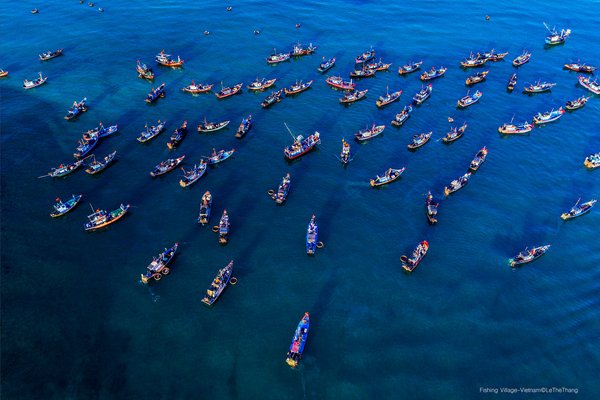 Hình ảnh toàn cảnh trên không của một làng chài với nhiều thuyền đánh cá trên biển xanh. Cảnh biển rộng lớn và yên bình tạo cảm giác thư thái và tĩnh lặng.
