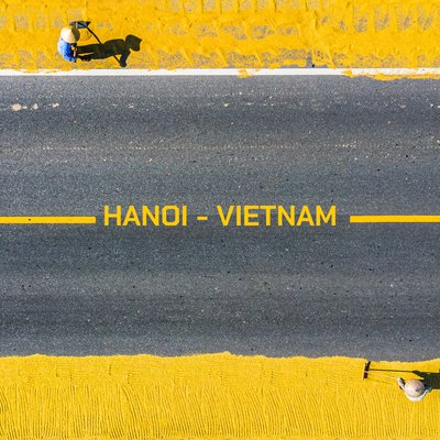 Bức ảnh chụp từ trên cao cho thấy cảnh phơi thóc trên hai bên đường nhựa với hai người đang làm việc. Hình ảnh tạo cảm giác yên bình và thể hiện nét đẹp trong cuộc sống nông thôn kết hợp với đô thị.