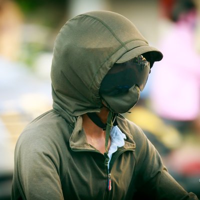 Hình ảnh một người đàn ông mặc áo hoodie và đeo khẩu trang cùng mũ bảo hiểm trên đường phố thành phố. Bức ảnh tạo cảm giác yên bình và tập trung vào cuộc sống hàng ngày trong môi trường đô thị.