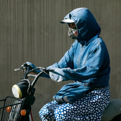 Hình ảnh một người mặc áo khoác denim và quần chấm bi đang ngồi trên xe máy trên nền tường xám trong ánh sáng tự nhiên. Bức ảnh tạo cảm giác yên bình và tập trung vào sự đơn độc giữa không gian thành thị.