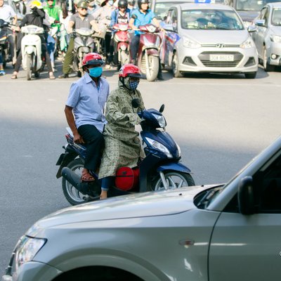 Hình ảnh một giao lộ đông đúc tại thành phố với nhiều xe máy và ô tô đang chờ đèn đỏ. Không khí có vẻ bình thường và yên tĩnh, phản ánh cuộc sống hàng ngày tại đô thị.