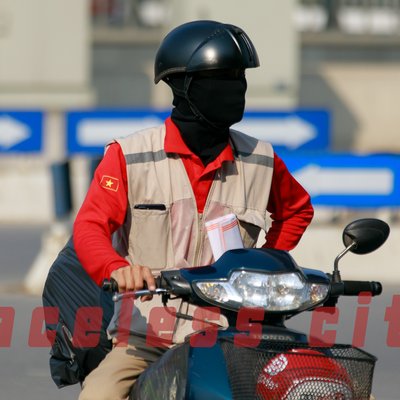 Hình ảnh một người đi xe máy trong thành phố, mặc áo đỏ và đội mũ bảo hiểm cùng khẩu trang che kín mặt. Cảnh vật thể hiện sự yên tĩnh và tập trung trong một khoảnh khắc giao thông đô thị.