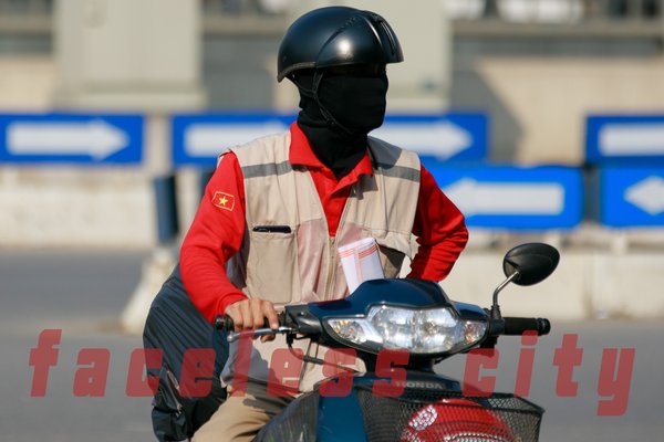 Hình ảnh một người đi xe máy trong thành phố, mặc áo đỏ và đội mũ bảo hiểm cùng khẩu trang che kín mặt. Cảnh vật thể hiện sự yên tĩnh và tập trung trong một khoảnh khắc giao thông đô thị.