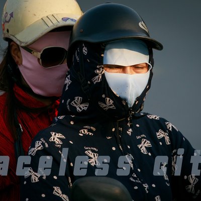 Bức ảnh chụp hai người trên xe máy trong trang phục bảo hộ với khẩu trang và mũ bảo hiểm, thể hiện cảnh đi lại trong thành phố. Cảm giác tổng thể là sự an toàn và bảo vệ trong môi trường đô thị có ô nhiễm.