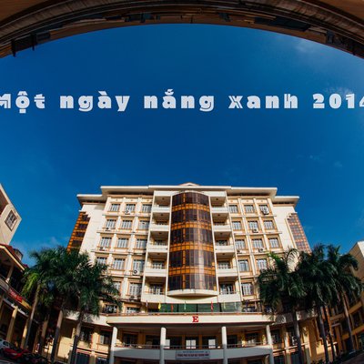 Bức ảnh chụp một toà nhà đại học trong thành phố với bầu trời xanh và cây cọ bao quanh. Không gian tạo cảm giác yên bình và tươi sáng dưới ánh nắng ban ngày.