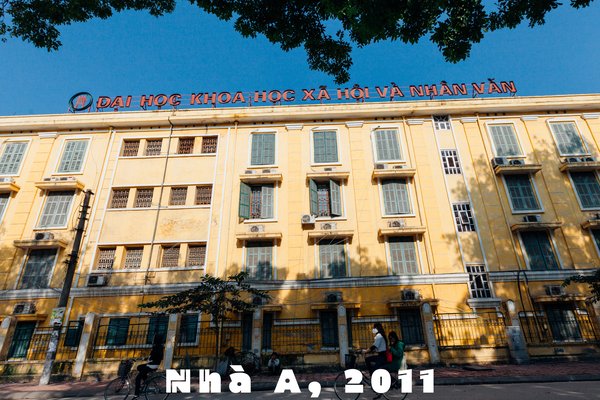 Bức ảnh chụp một toà nhà đại học tại Hà Nội với người đi xe đạp trên đường phố phía trước. Cảnh vật tạo cảm giác yên bình và sinh động của cuộc sống đô thị buổi sáng.