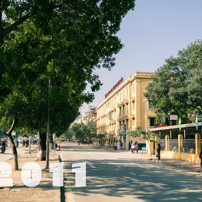 Hình ảnh đường Nguyễn Trãi tại Hà Nội với nhiều cây xanh, người đi bộ và xe máy trên đường. Không khí buổi sáng tạo cảm giác yên bình và nhộn nhịp của cuộc sống đô thị.