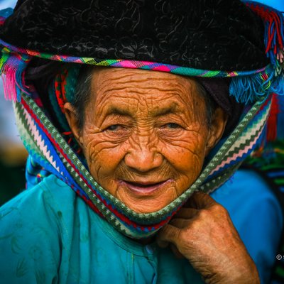 Bức ảnh chụp chân dung một bà lão người Mông mặc trang phục truyền thống màu xanh với ánh sáng tự nhiên. Hình ảnh thể hiện sự giàu có về văn hoá và truyền thống của người dân tộc thiểu số vùng cao nguyên đá.