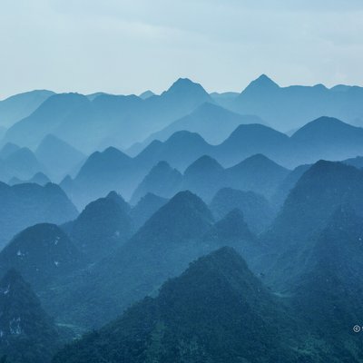 Bức ảnh chụp cảnh cao nguyên đá với các ngọn núi và đồi xanh mờ ảo trong sương mù. Khung cảnh tạo cảm giác bình yên và tĩnh lặng, mang lại sự thư thái cho người xem.