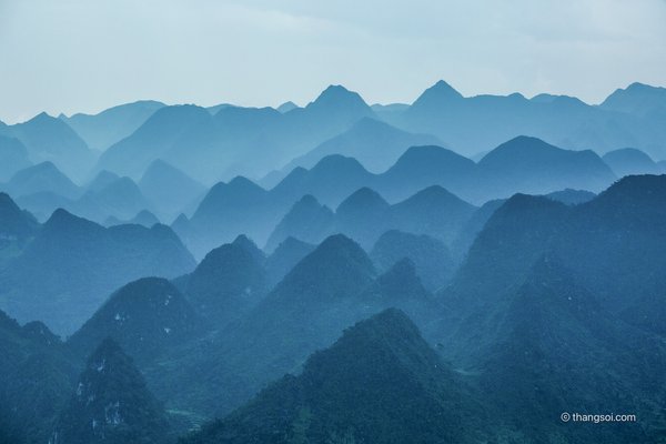 Bức ảnh chụp cảnh cao nguyên đá với các ngọn núi và đồi xanh mờ ảo trong sương mù. Khung cảnh tạo cảm giác bình yên và tĩnh lặng, mang lại sự thư thái cho người xem.