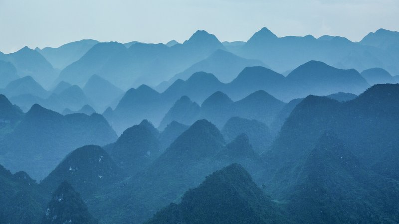 Bức ảnh chụp cảnh cao nguyên đá với các ngọn núi và đồi xanh mờ ảo trong sương mù. Khung cảnh tạo cảm giác bình yên và tĩnh lặng, mang lại sự thư thái cho người xem.